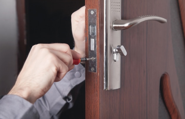 Mężczyzna naprawy zamka drzwi. Ręka mechanika ze śrubokrętem