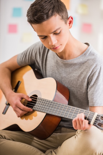 Mężczyzna nastolatek siedzi w domu i gra na gitarze.