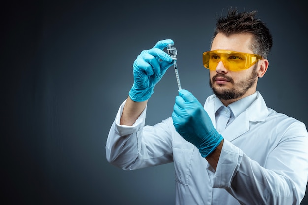 Mężczyzna naukowiec, asystent laboratoryjny w białym fartuchu i okularach trzyma w rękach butelkę ze szczepionką, badania medyczne, laboratorium, eksperymenty. Analiza chemiczna szczepień.