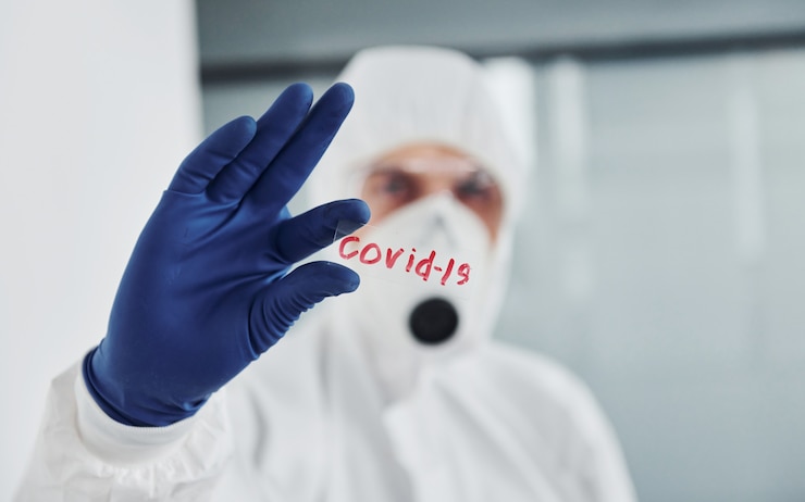 Zdjęcie mężczyzna naukowiec w fartuchu, okularach i masce obronnej trzyma szklankę z napisem covid-19