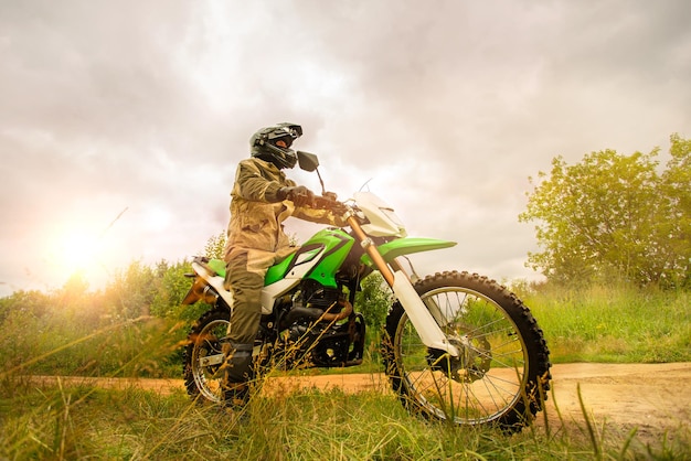 Mężczyzna nosi kask motocyklowy i mundur bezpieczeństwa, siedząc na rowerze brudu na zewnątrz, piękny malowniczy krajobraz na tle w warunkach dziennych. Koncepcja motocrossu.