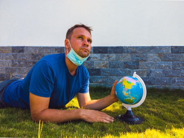 Mężczyzna noszący maskę trzymającą w ręku mapę świata kuli ziemskiej Poddaj się kwarantannie, aby chronić rozprzestrzeniającego się wirusa Kiedy możesz znowu podróżować Epidemia pandemiczna koronawirus 2019ncov sars covid19 koncepcja wirusa