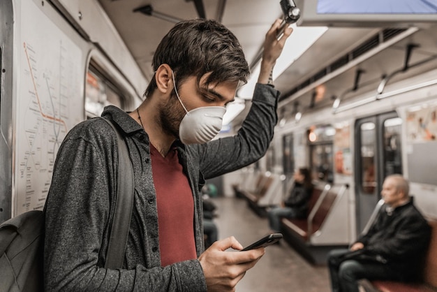 Mężczyzna noszący maskę za pomocą smartfona w pociągu Skytrain lub metrze Koncepcja opieki zdrowotnej