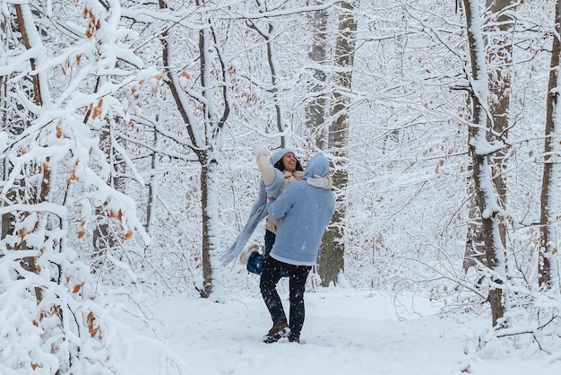Mężczyzna obraca kobietę w ramionach w zimowym lesie
