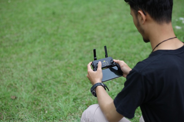 Mężczyzna obsługujący lub nawigujący dronem za pomocą pilota w zielonym parku Pilot drona