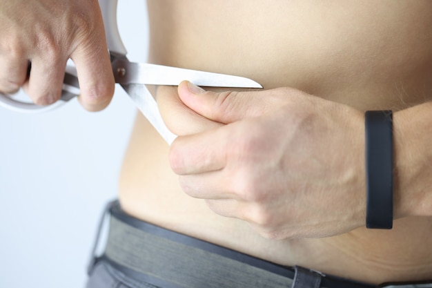 Mężczyzna odcina nadmiar skóry tłuszczem z brzucha za pomocą diety nożycowej i koncepcji odchudzania