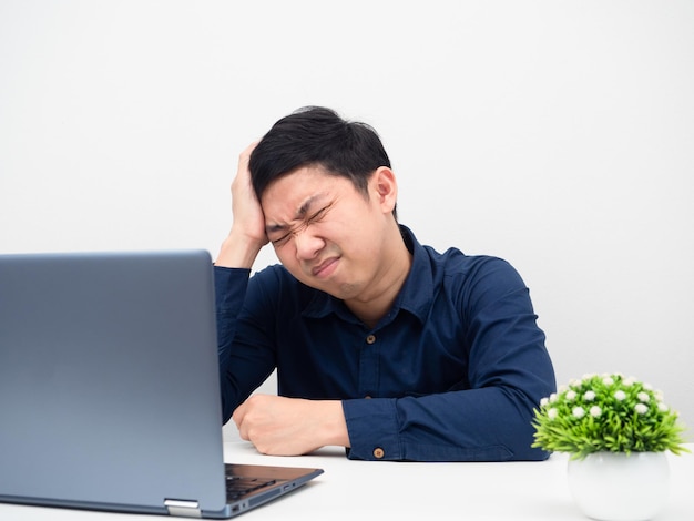 Mężczyzna odczuwa ból głowy z powodu swojej pracy, siedząc przy stole z laptopem na białym tle