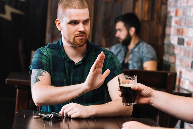 Mężczyzna odmawiający napój alkoholowy oferowany przez jego przyjaciela w barze