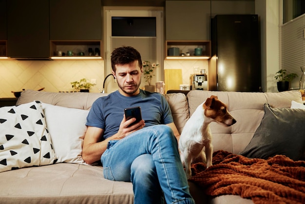 Mężczyzna odpoczywa na kanapie z psem i używa smartfona