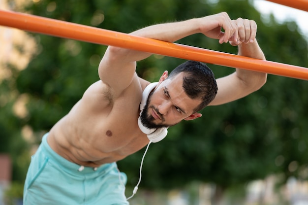 Mężczyzna odpoczywa po wykonaniu push UPS na barach na zewnątrz w ciągu dnia