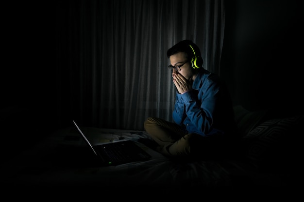 Mężczyzna ogląda telewizję w laptopie siedzi na łóżku w nocy w domu