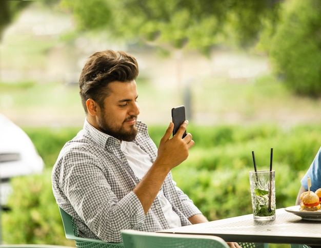 Mężczyzna oglądający smartfon siedzący na tarasie kawiarni