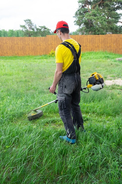 Zdjęcie mężczyzna ogrodnik kosi zieloną trawę trawnika na podwórku za pomocą kosiarki benzynowej trymer do pielęgnacji działki ogrodowej