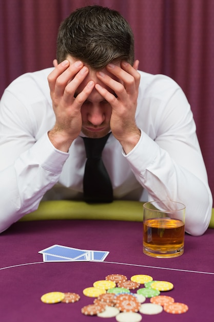 Mężczyzna opiera na pokerowym stole patrzeje martwiący się w kasynie