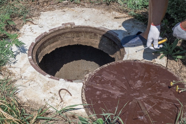 Mężczyzna otworzył pokrywę włazu studni. Sprawdzanie i instalacja wodomierza.