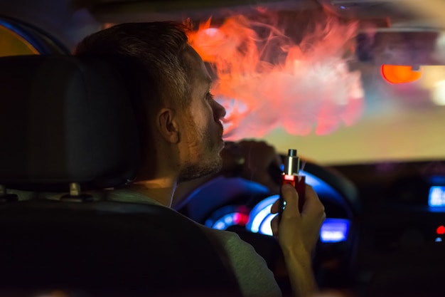 Mężczyzna pali elektronicznego papierosa w samochodzie. Wieczorna pora nocna