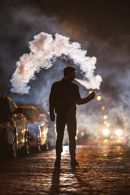 Mężczyzna pali elektroniczny papieros na ulicy. Wieczorna pora nocna