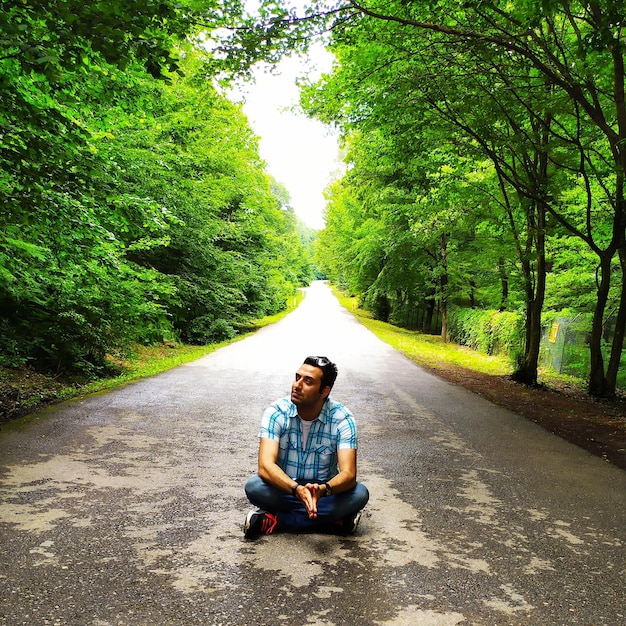Zdjęcie mężczyzna patrzący w stronę, siedząc na drodze przeciwko drzewom