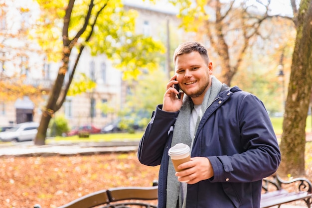 Mężczyzna pijący kawę na zewnątrz w sezonie jesiennym rozmawia przez telefon