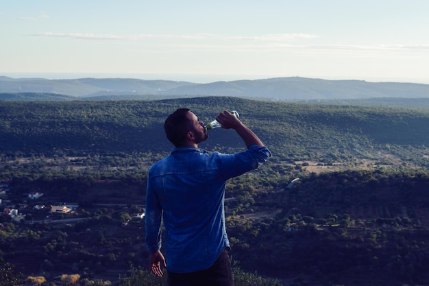 Zdjęcie mężczyzna pije z butelki, stojąc na krajobrazie przeciwko niebu