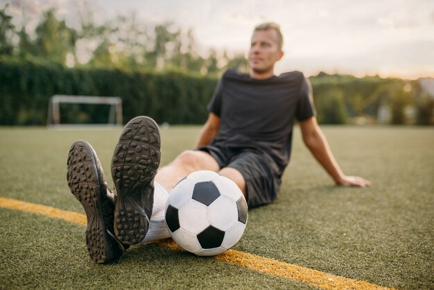 Zdjęcie mężczyzna piłkarz z piłką, siedząc na trawie na boisku. piłkarz na stadionie zewnętrznym, trening przed meczem, trening piłki nożnej