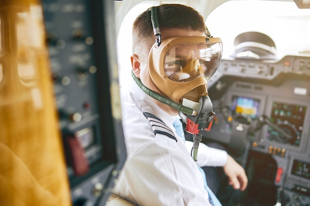 Mężczyzna pilot nosić maskę powietrzną w kokpicie samolotu pasażerskiego. Nowoczesny samolot z deską rozdzielczą i nawigacją powietrzną. Europejczyk nosi mundur. Cywilne lotnictwo komercyjne. Koncepcja podróży lotniczych