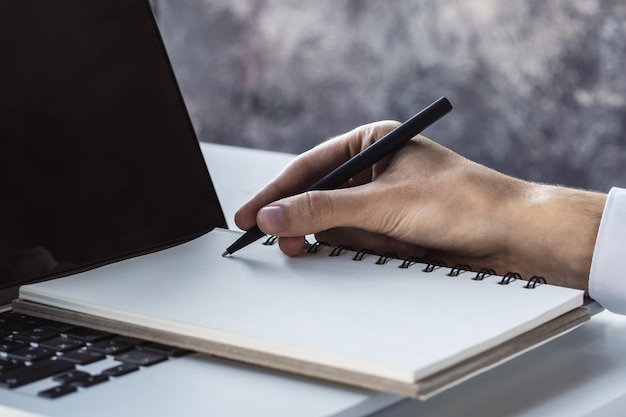 Mężczyzna pisze piórem w dzienniku na klawiaturze laptopa w słonecznym biurze biznesu i edukacji koncepcja Close Up