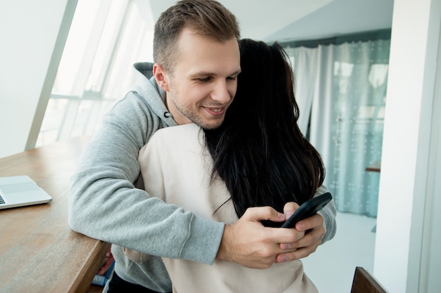 Mężczyzna Pisze Sms-a Do Innych Kobiet, Gdy Obejmuje Swoją Dziewczynę. Koncepcja Oszustwa. Kobieta Ufa Mężowi, Ale On Ją Oszukuje. Biały Pokój Na Tle. Para Przytulania. Kłamstwa Zawsze Będą Się Pojawiać.