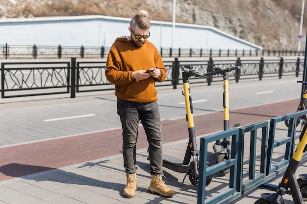 Mężczyzna płaci za skuter elektryczny za pomocą płatności internetowej za pomocą swojego telefonu komórkowego nowoczesnego transportu miejskiego