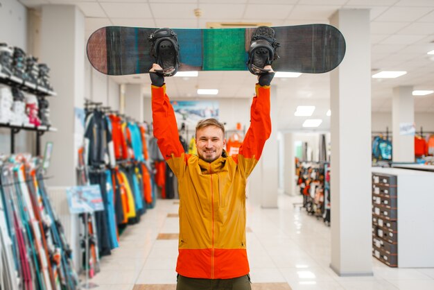 Mężczyzna podniósł deskę na snowboard, zakupy w sklepie sportowym.