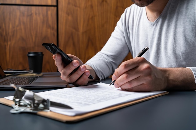 Mężczyzna podpisujący umowę dwukrotnie sprawdzający szczegóły w telefonie komórkowym Koncepcja wchodzenia w moc prawną do zaciągania zobowiązań Noszenie na co dzień