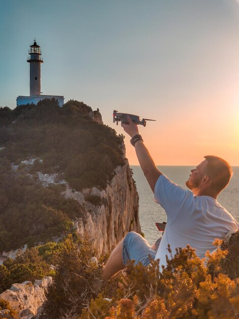 Mężczyzna podróżnik na klifie cieszący się zachodem słońca nad morzem latarnia morska wyspa lefkada strzelająca dronem