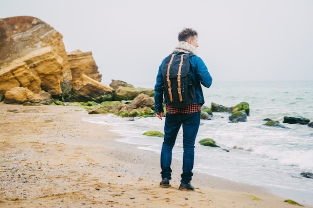 Mężczyzna podróżnik z plecakiem stojący na skale na tle pięknego morza z falami