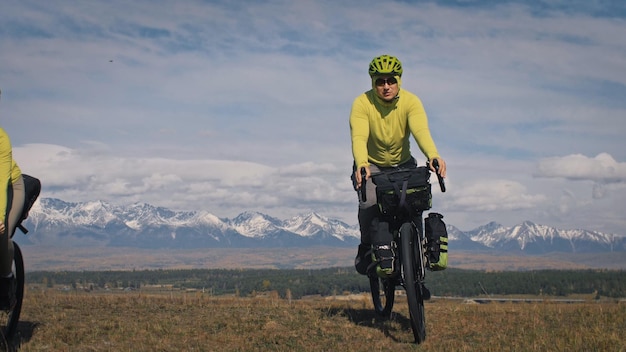 Zdjęcie mężczyzna podróżuje po mieszanym terenie rowerowe wycieczki rowerowe z bikepackingiem podróżnik podróż z torbami rowerowymi turystyka sportowa bikepacking rower odzież sportowa w kolorach zielono-czarna góra śnieżna czapka