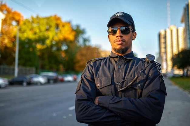 Mężczyzna policjant w mundurze i okularach przeciwsłonecznych na zewnątrz. Policjant chroni prawo. Policjant pracuje nad ulicami miasta, kontrolą porządku i sprawiedliwości