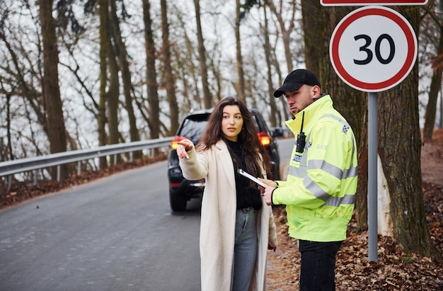 Zdjęcie mężczyzna policjant w zielonym mundurze rozmawia z właścicielką samochodu na drodze.