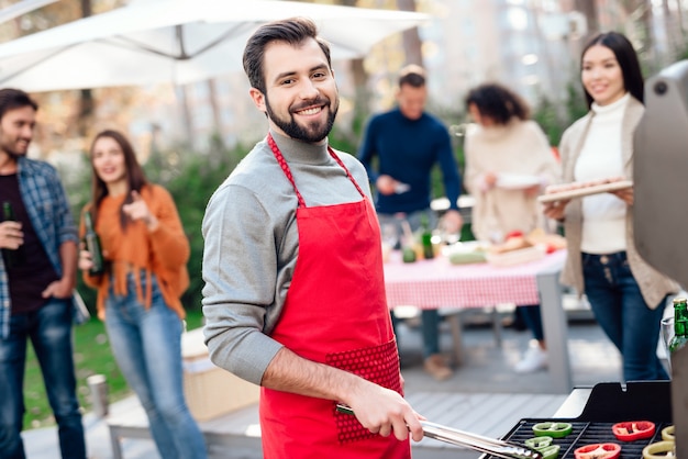 Mężczyzna pozuje na kamerze podczas gdy gotujący jedzenie na grillu.