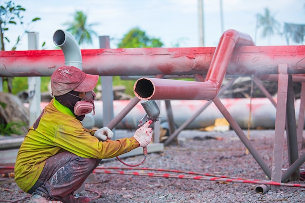 Mężczyzna pracownik posiadający przemysłowy pistolet natryskowy używany do powierzchni rurociągu na stalowym malowaniu przemysłowym i powlekaniu.