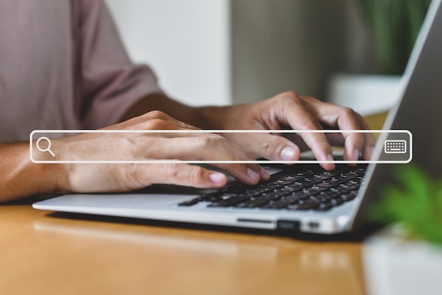 Mężczyzna pracujący na biurku w domu, ręka na klawiaturze z ikoną paska wyszukiwania, używa technologii do wyszukiwania informacji w Internecie
