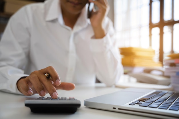 Mężczyzna pracujący na biurku za pomocą kalkulatora do obliczania liczb i raportu biznesowego rozmawia inteligentny telefon na koncepcji rachunkowości finansowej biurka