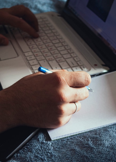 Mężczyzna pracujący na laptopie i piszący notatki w notatniku