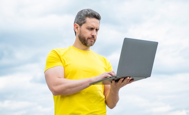 Mężczyzna pracujący online na laptopie na tle nieba biznes online