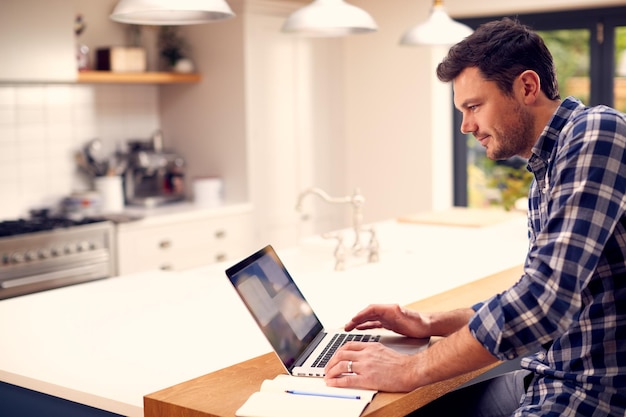 Mężczyzna pracujący w domu przy użyciu laptopa na blacie kuchennym
