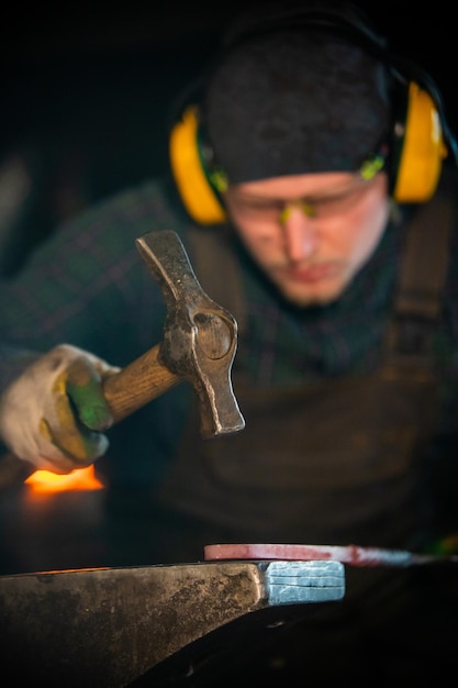 Mężczyzna pracujący w kowalu, wyrabiający detal z gorącego metalu za pomocą młotka