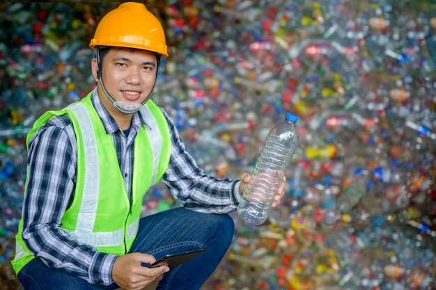 Mężczyzna pracujący w zakładzie recyklingu trzyma plastikowe butelki i tabletki, aby wyrzucić i poddać recyklingowi plastikowe butelki w małym zakładzie recyklingu odpadów