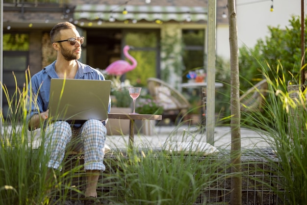 Mężczyzna pracuje na laptopie siedząc na podwórku