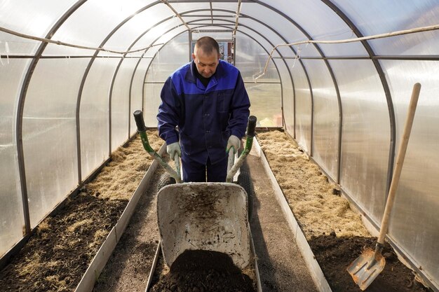 Mężczyzna pracuje w ogrodzie warzywnym na wczesną wiosnę kopa ziemię pracuje w szklarni