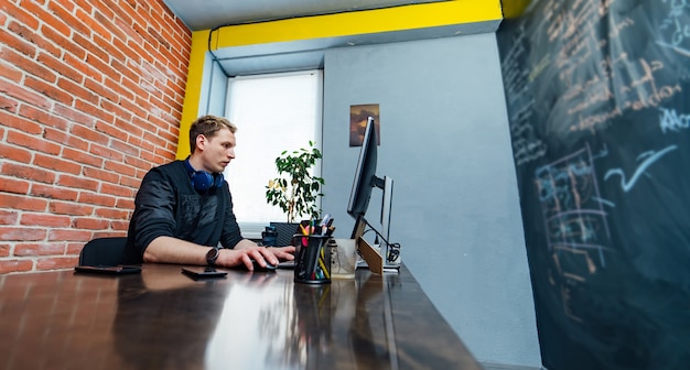 Zdjęcie mężczyzna programista pracujący na komputerze stacjonarnym w pobliżu monitora w biurze w firmie zajmującej się tworzeniem oprogramowania. technologie programowania i kodowania stron internetowych.