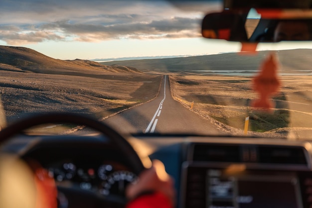 Mężczyzna prowadzący samochód przez pustynię na asfaltowej drodze o zachodzie słońca