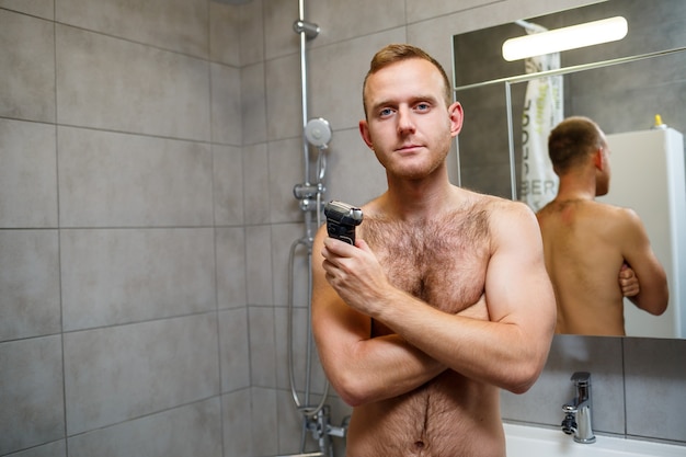 Mężczyzna przed lustrem goli twarz elektryczną maszynką do golenia. Podrażnienie skóry. Procedura kąpieli